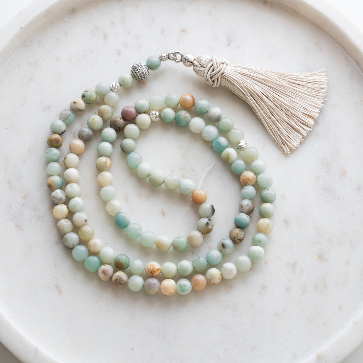 Tasbih (Misbaha) aus Amazonit mit 99 Natursteinperlen, silbernen Zwischenperlen und cremefarbener Quaste auf weißem Marmor