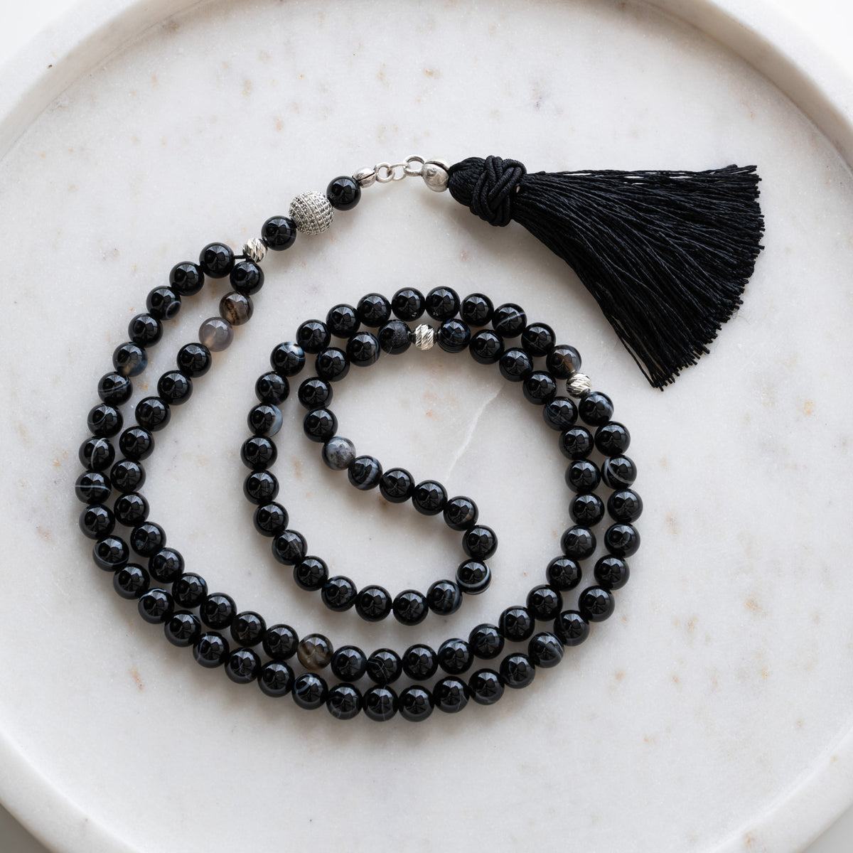 Tasbih (misbaha) i sort agat med 99 naturlige perler, skilleperler i sølv og en sort kvast på hvid marmor