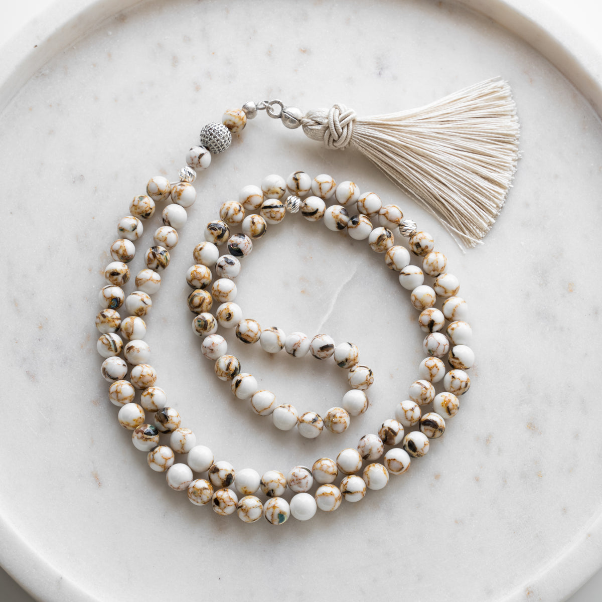 Tasbih (Misbaha) aus Karamell-Quarz mit 99 Natursteinperlen, silbernen Zwischenperlen und cremefarbener Quaste auf weißem Marmor