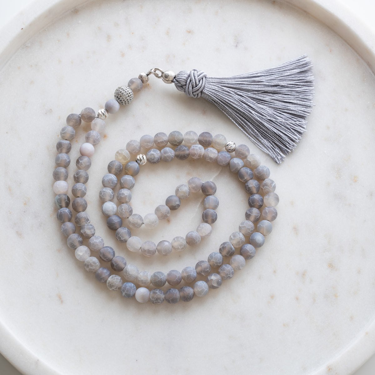 Tasbih (misbaha) i mat grå agat med 99 naturlige perler, skilleperler i sølv og en grå kvast på hvid marmor